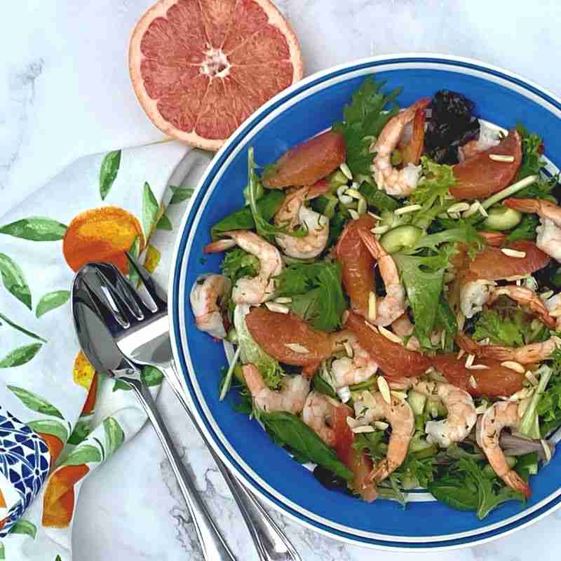 prawn and red grapefruit salad with almonds in blue bowl with grapefruit half and salad servers