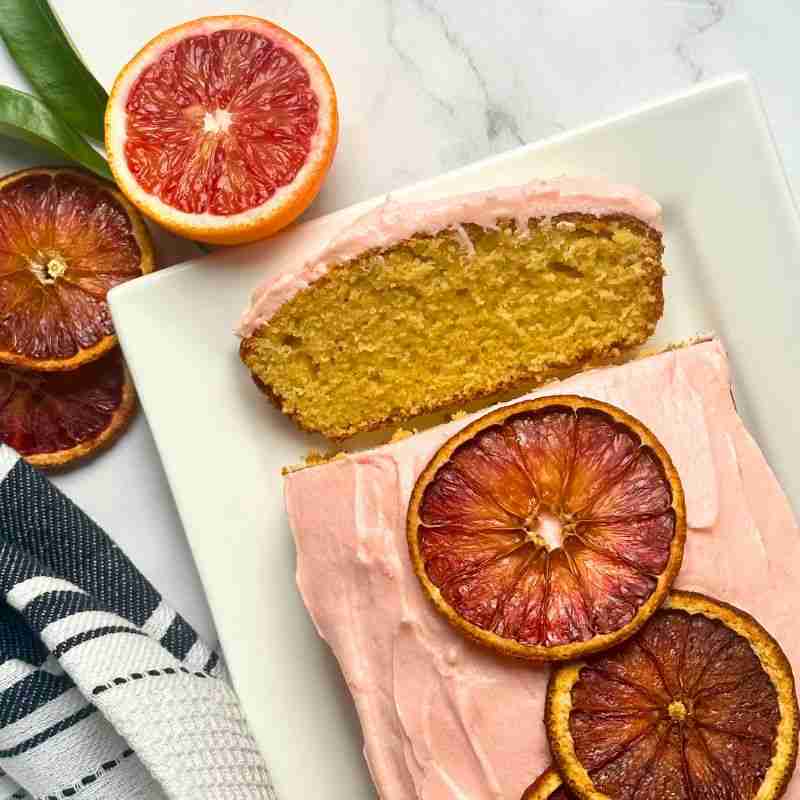 blood orange loaf cake on white dish with fresh blood oranges