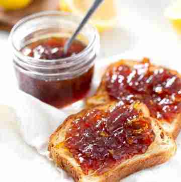 Lemon honey marmalade in glass jar with spoon and spread on slices of toast