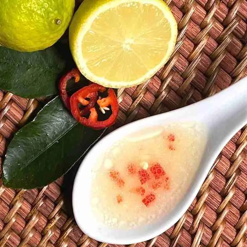 lime and chili (chilli) salad dressing in a white ceramic spoon with fresh limes and chili slices