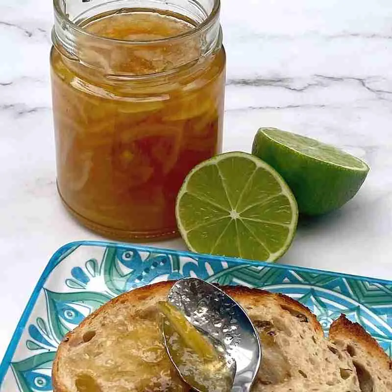 lime marmalade in a glass jar with fresh lime halves and marmalade on toast on a blue and green plate