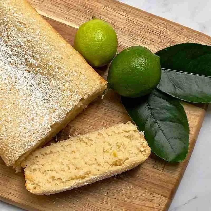 vegan coconut and lime loaf cake on wooden board with 2 fresh limes and lime leaves