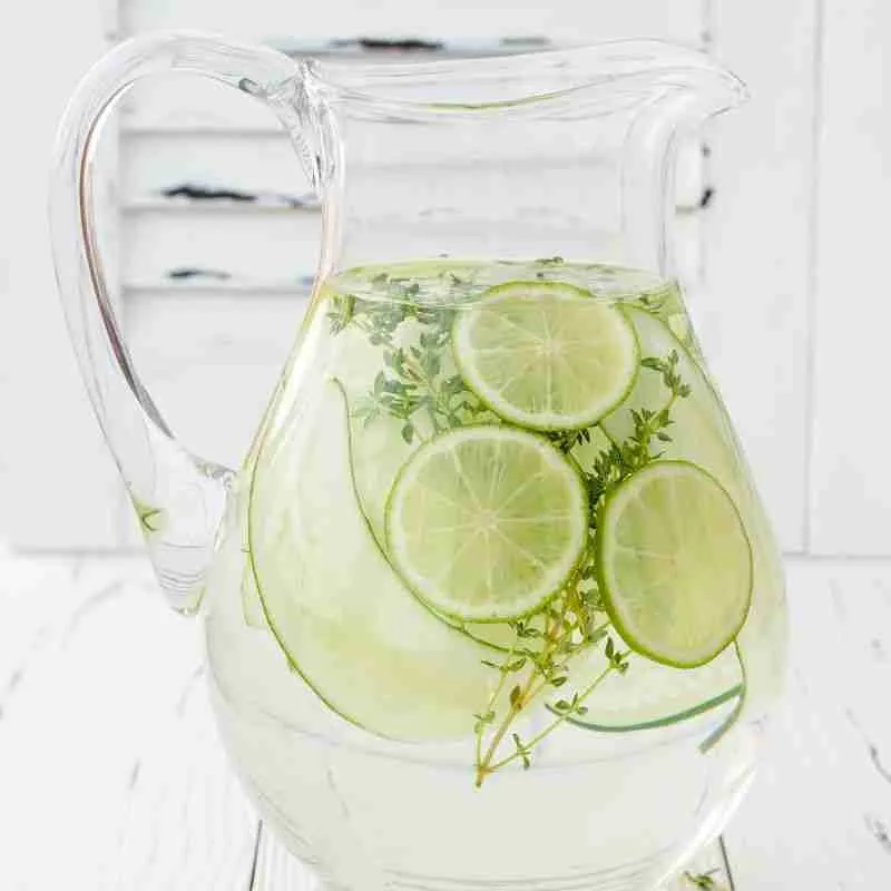 Lime and cucumber slices with herbs in water in a glass jug