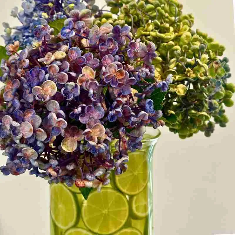 blue, purple and green hydrangeas in a glass vase decorated with slices of lime