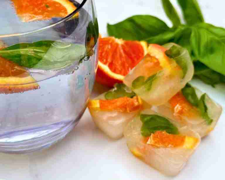 blood orange and basil ice cubes with glass of sparkling water and fresh orange and basil