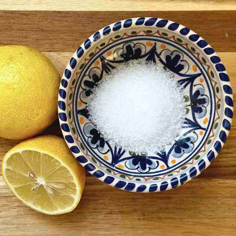 small patterned bowl of salt and fresh lemons on wooden chopping board
