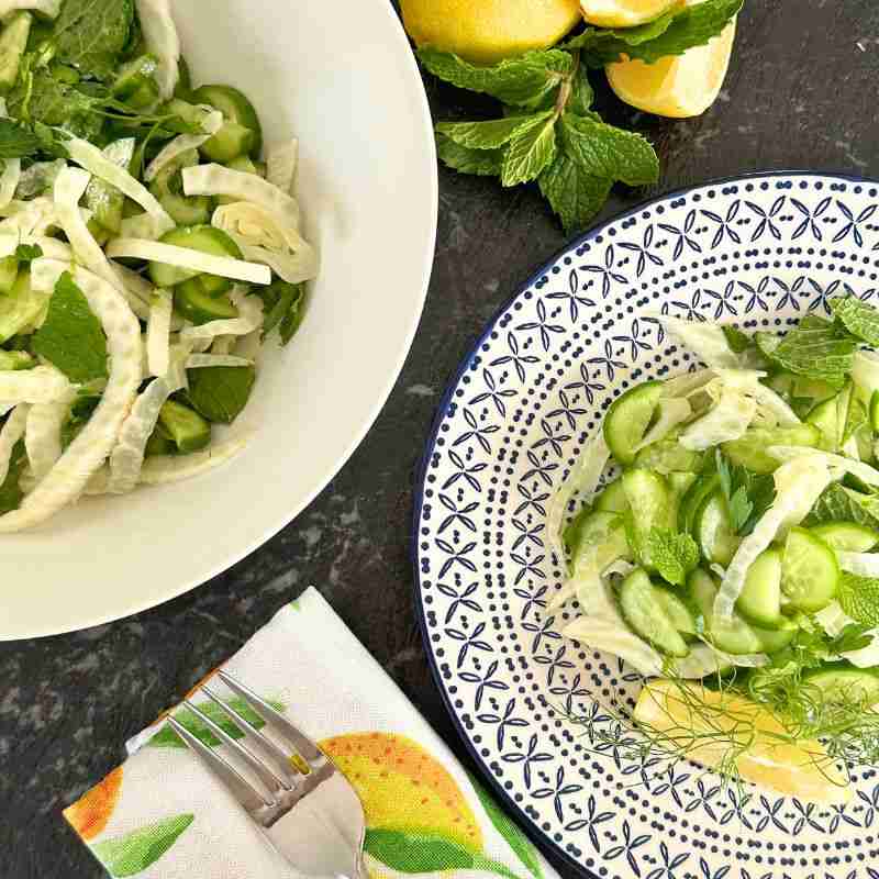 lemon fennel and cucumber salad on blue and white plate with fresh lemons and mint