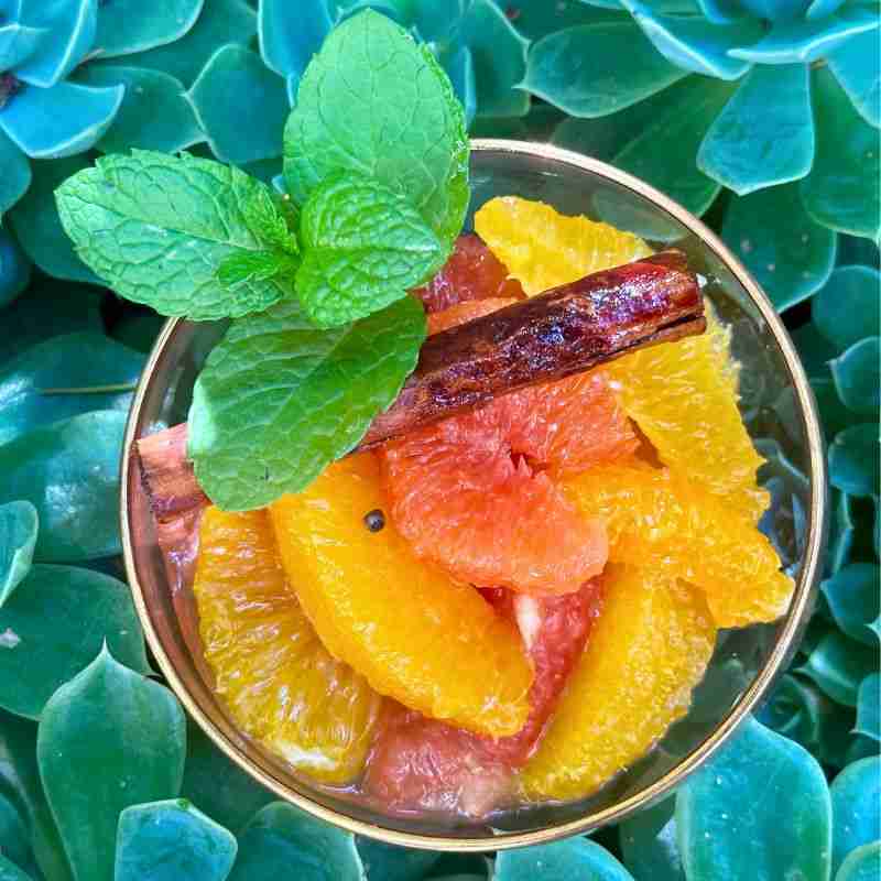 citrus fruit salad in glass bowl with mint and cinnamon stick surrounded by green succulent leaves