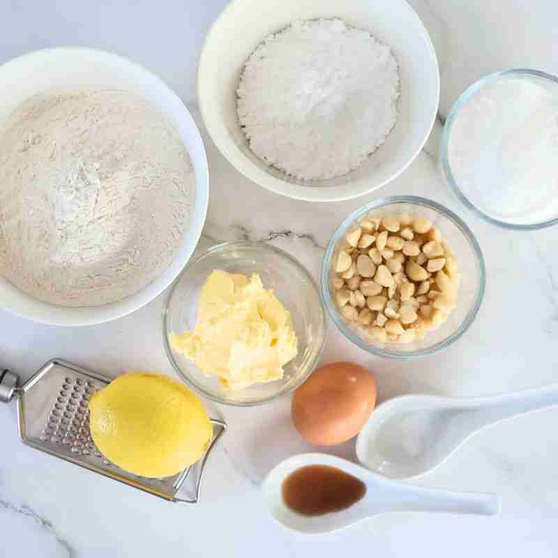 lemon macadamia cookie ingredients including self raising flour, powdered sugar, caster sugar, butter, egg, chopped macadamia nuts, lemon zest and juice, vanilla and salt