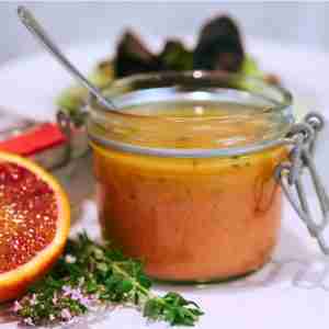 blood orange vinaigrette salad dressing in glass jar with fresh thyme and orange half