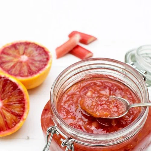 blood orange and rhubarb jam in glass jar with spoon and fresh blood oranges