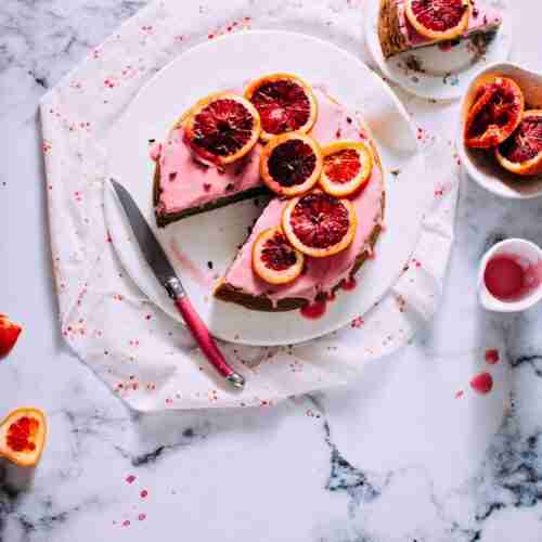 blood oramge cake with pnk icing on a white plate with fresh blood oranges