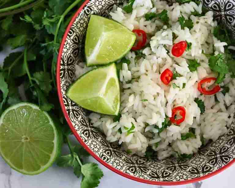 coconut and lime rice with cilantro and chile in a black and white bowl with fresh lime
