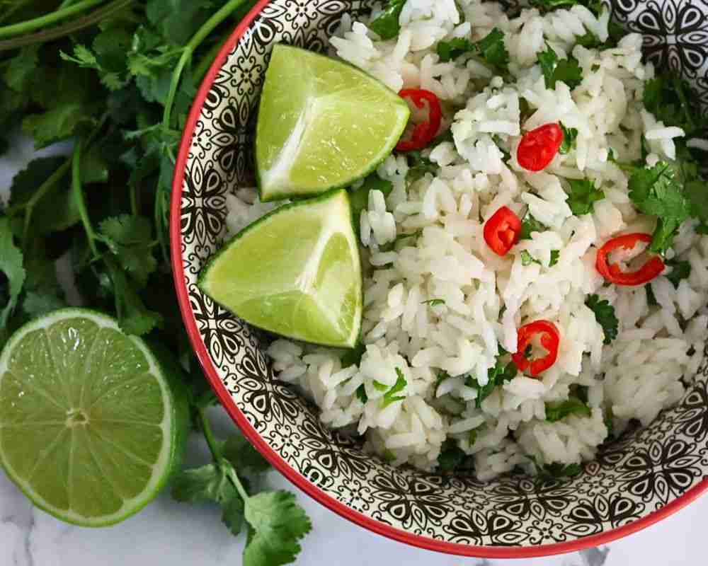 coconut and lime rice with cilantro and chile in a black and white bowl with fresh lime