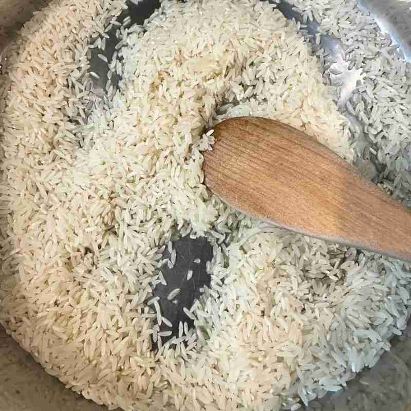 rice in frying pan with olive oil being stirred with wooden spoon