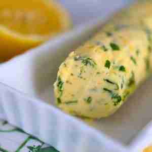 compound lemon garlic butter with herbs in a white dish with fresh lemon