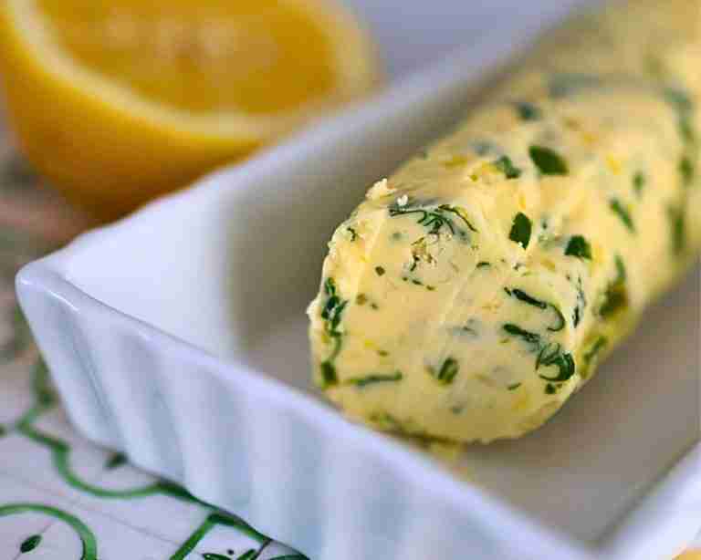 compund lemo garlic buttter with herbs in white dish with fresh lemon half