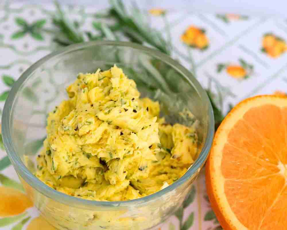 compund orange butter with pepper and rosemary in glass dish with fresh rosemary and orange half