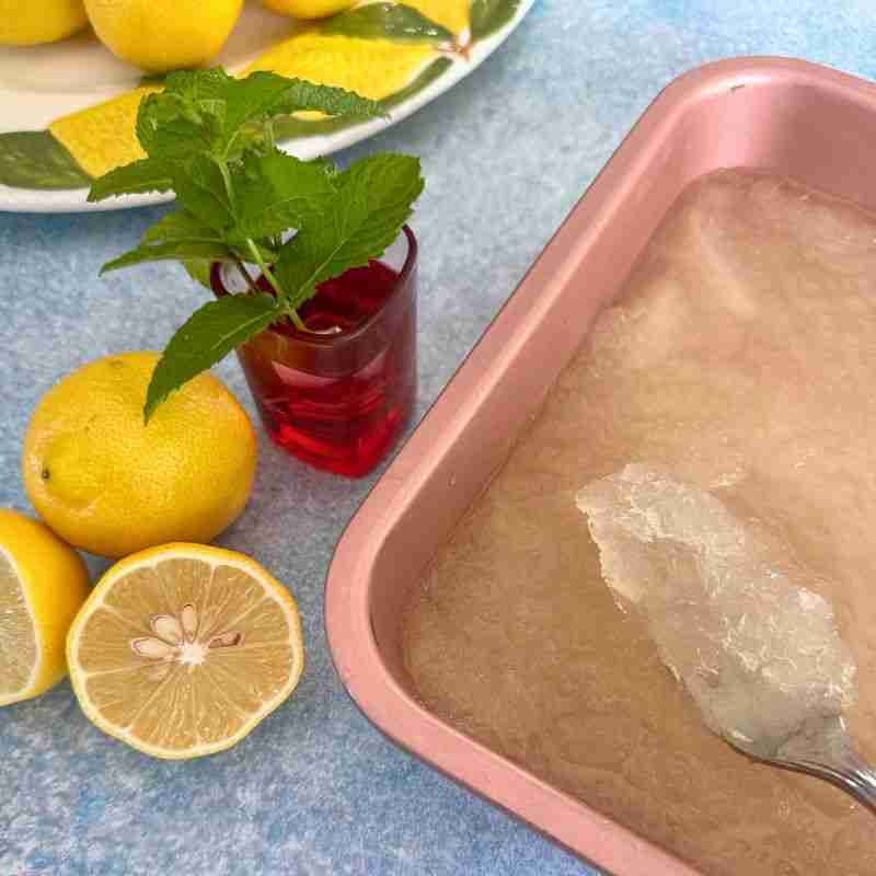 using a fork to make lemon granita in a metal baking pan with fresh lemons and mint