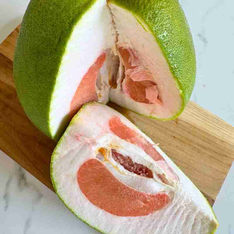 fresh pomelo on wooden chopping board cut to show pink flesh inside